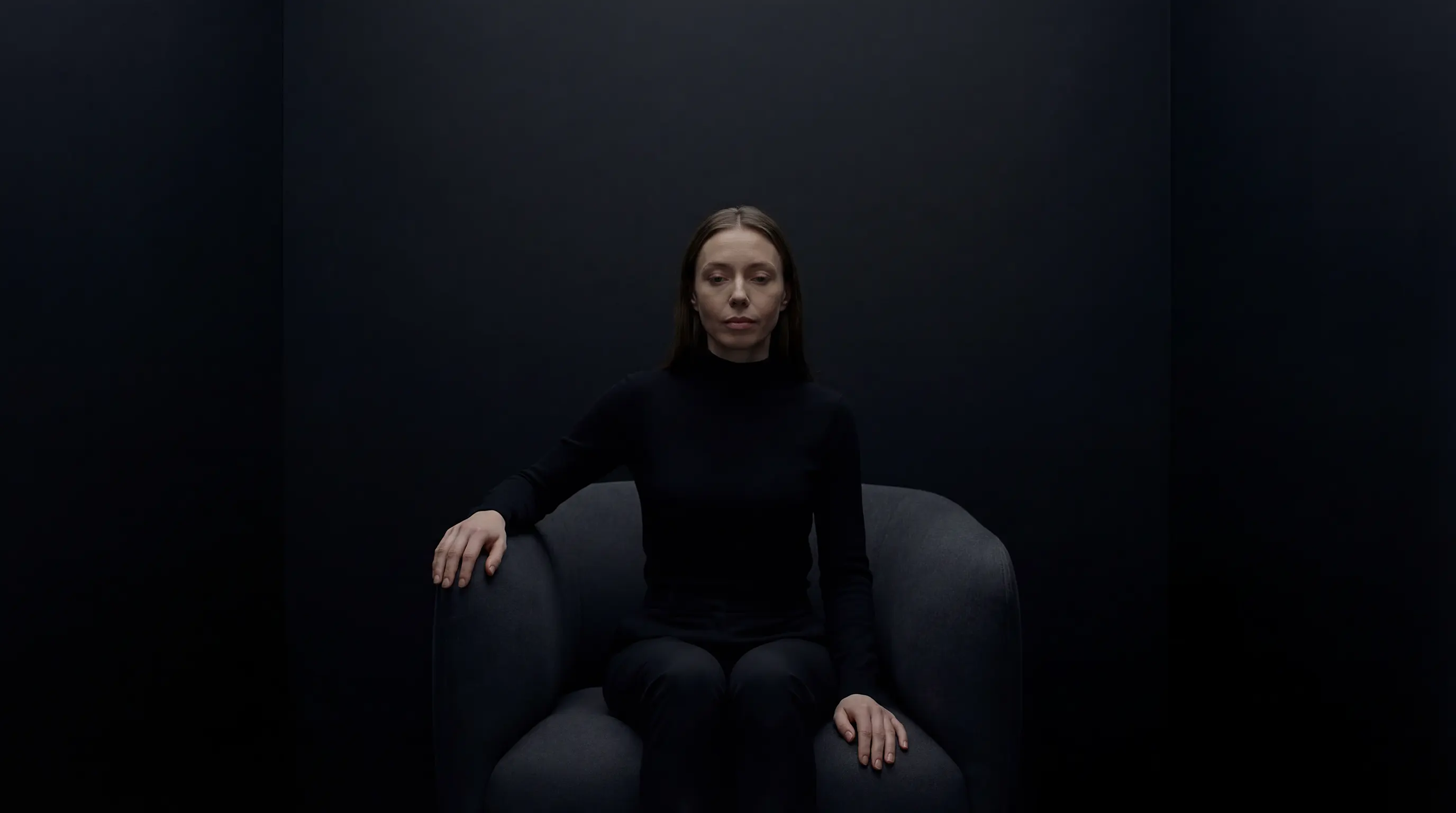 Mujer sentada en una butaca dentro de un espacio oscuro y silencioso.